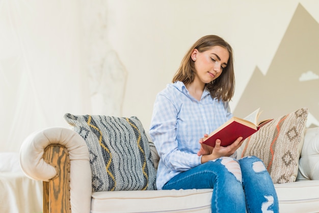 Mujer sentada en la sala de estar en el sofá leyendo el libro