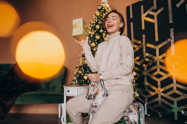 Mujer sentada en una silla pony de madera junto al árbol de navidad