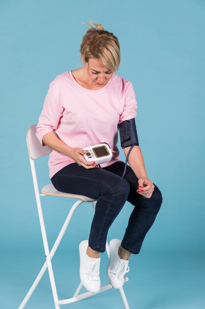 Mujer sentada en una silla que controla la presión sanguínea en un tonómetro eléctrico