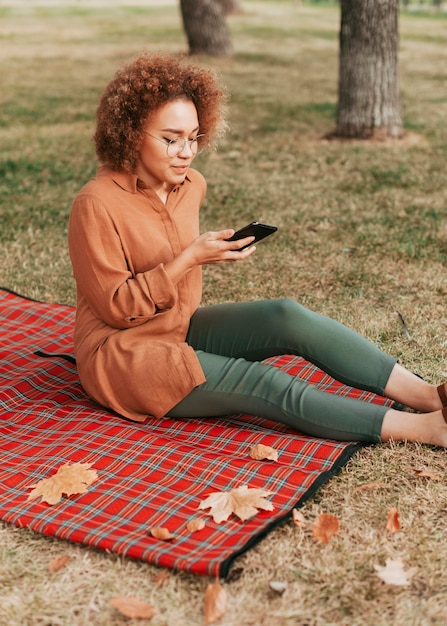 Mujer sentada sobre una manta de picnic mientras revisa su teléfono