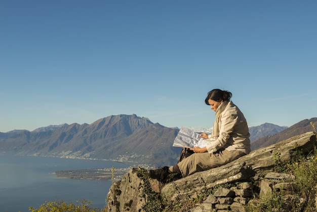 Mujer sentada sobre la roca con una hermosa vista de una montaña cerca de la orilla del mar