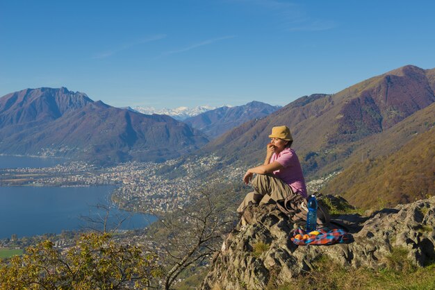 Mujer sentada sobre la roca con una hermosa vista de las montañas cerca de la orilla del mar