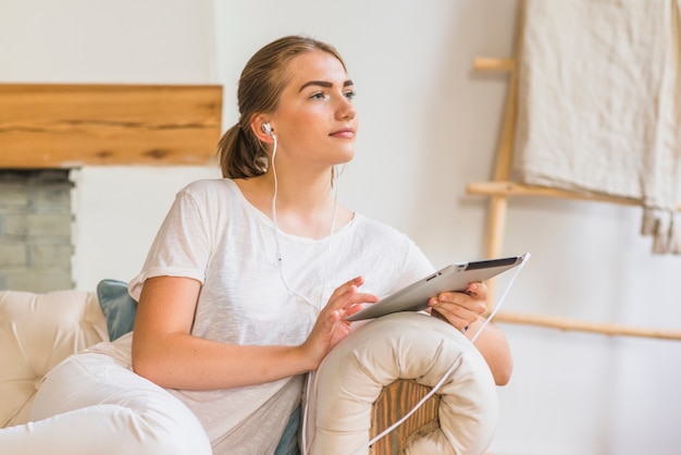 Mujer sentada en el sofá con auriculares y tableta digital