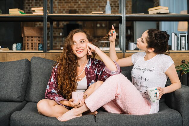 Mujer sentada en el sofá jugando con el pelo de su amiga