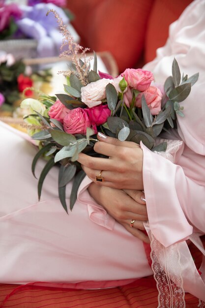 Mujer sentada y sosteniendo flores de la boda en la habitación en vestido largo rosa y tacones rojos.