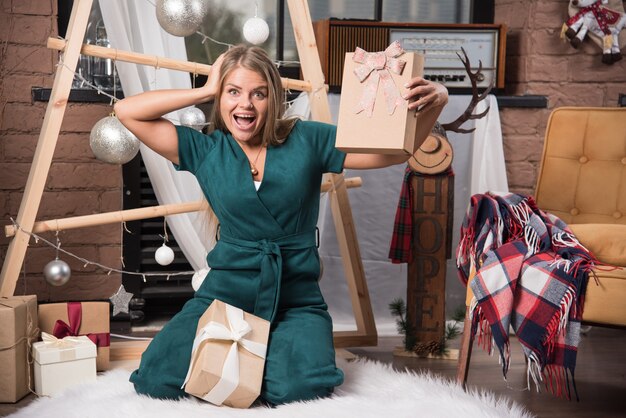 Mujer sentada en el suelo en casa con regalos de Navidad