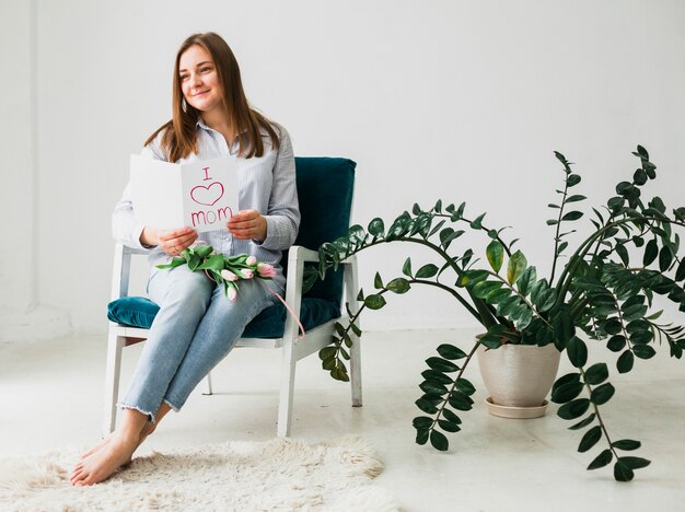 Foto gratuita mujer sentada con tarjeta de felicitación y flores