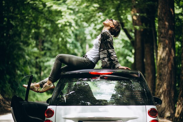 Mujer sentada en el techo del coche en el bosque