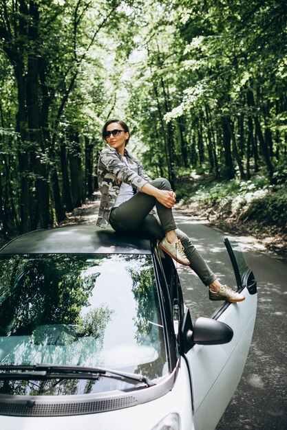 Mujer sentada en el techo del coche en el bosque