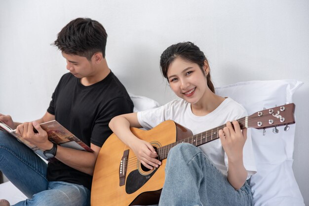 Una mujer sentada toca la guitarra y un hombre sosteniendo un libro y cantando.