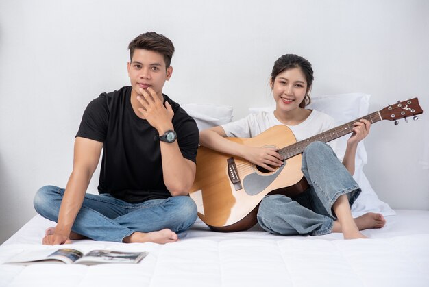 Una mujer sentada toca la guitarra y un hombre sosteniendo un libro y cantando.