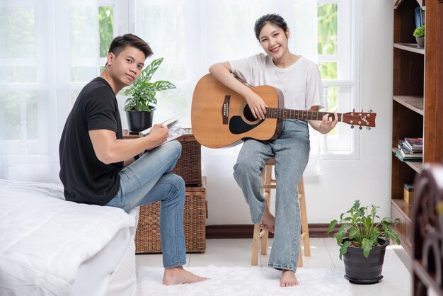 Una mujer sentada toca la guitarra y un hombre sosteniendo un libro y cantando.