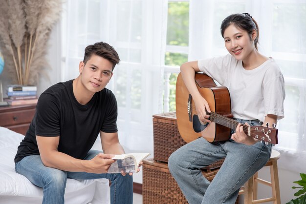 Una mujer sentada toca la guitarra y un hombre sosteniendo un libro y cantando.