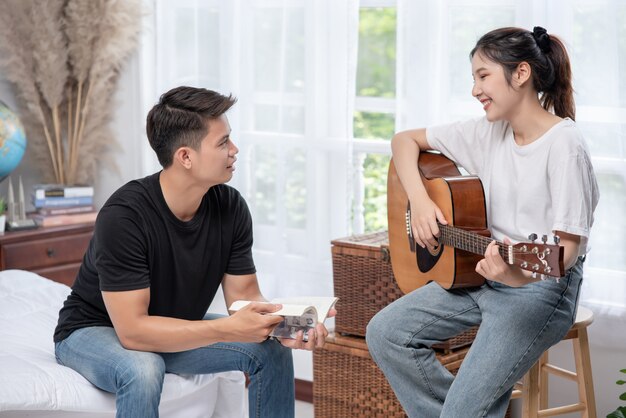 Una mujer sentada toca la guitarra y un hombre sosteniendo un libro y cantando.