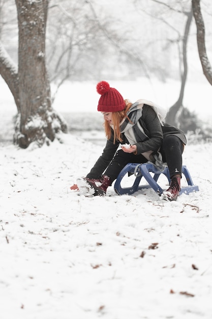 Foto gratuita mujer sentada en trineo y jugando con nieve