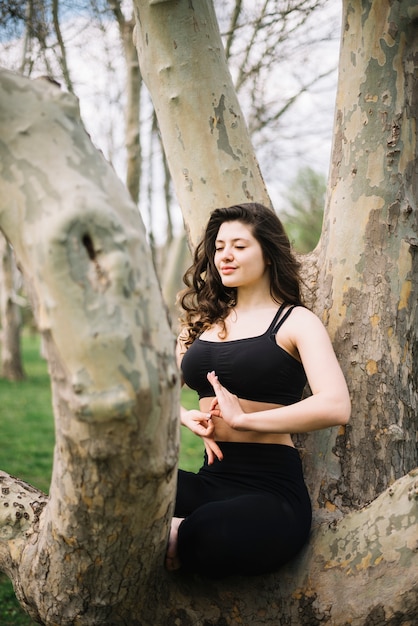 Mujer sentada en el tronco del árbol meditando con gesto mudra