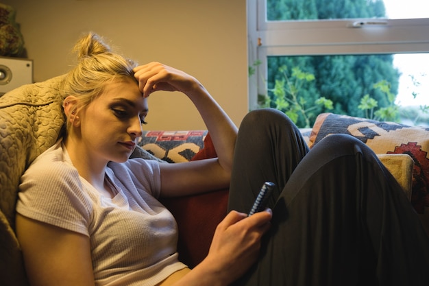 Mujer sentada y usando un teléfono móvil en el sofá en el salón
