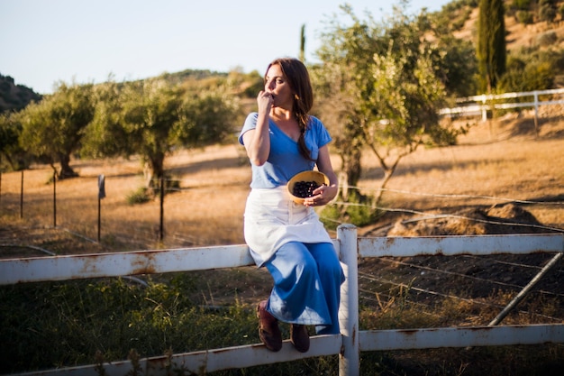 Foto gratuita mujer sentada en la valla comiendo bayas en el tazón