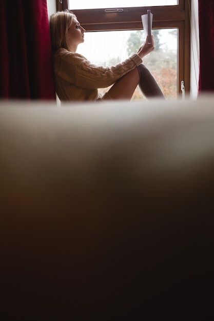 Foto gratuita mujer sentada en la ventana y leyendo un libro