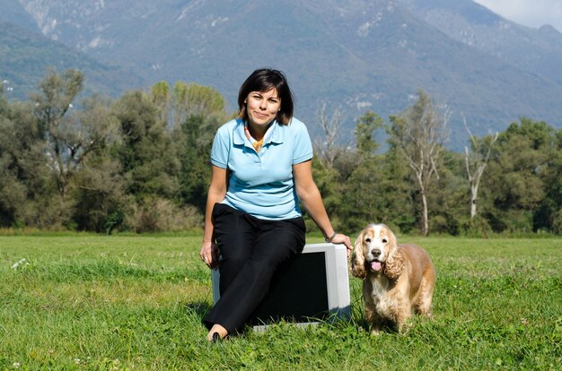 Mujer sentada en un viejo televisor en el campo con un cocker spaniel en el lateral