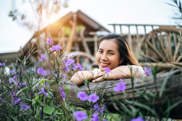 la mujer se sentó feliz en el jardín de flores y puso sus manos hacia la valla de madera