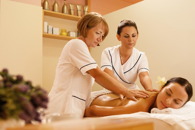 Mujer serena recibiendo masaje de espalda por dos terapeutas durante el tratamiento de spa