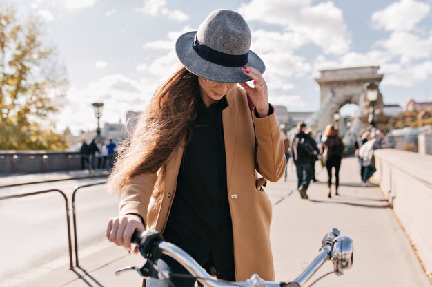 Mujer seria en abrigo beige de moda conduciendo por la ciudad en la mañana de otoño