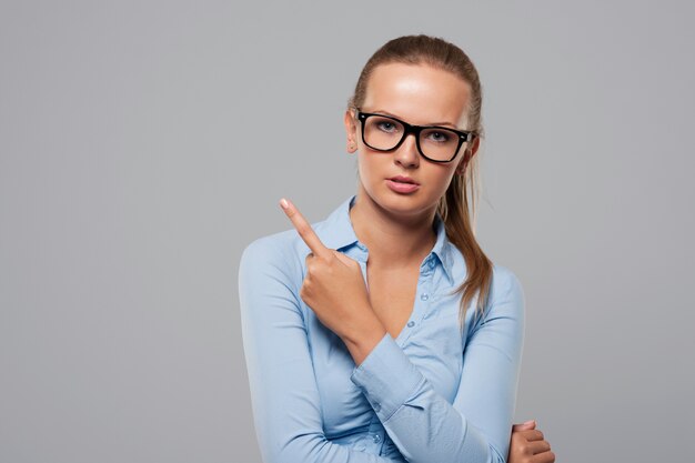 Mujer seria con gafas de moda apuntando al espacio de copia