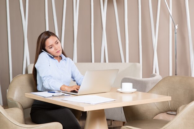 La mujer seria habla en el teléfono de trabajo en la computadora portátil