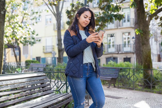 Mujer seria usando teléfono inteligente y de pie al aire libre