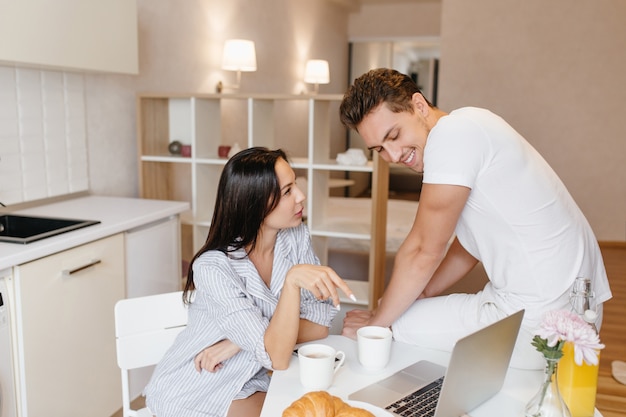 Mujer seria viste camisa masculina como pijama hablando con su novio en la cocina