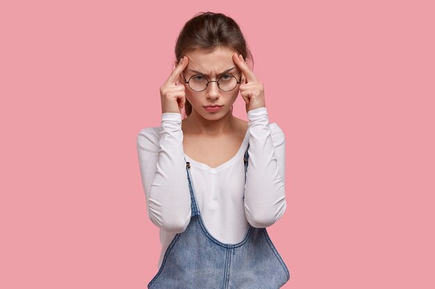 Una mujer seriamente disgustada intenta concentrarse y concentrarse en el trabajo, se toma las manos en las sienes, tiene un dolor de cabeza terrible, reduce el dolor de los analgésicos