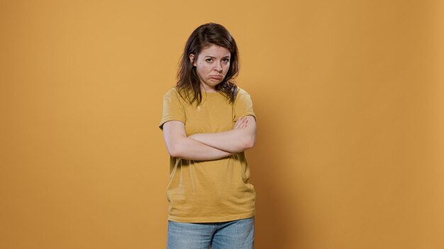 Mujer seriamente molesta con los brazos cruzados sintiéndose triste y decepcionada con un aspecto gruñón murmurando en el estudio. Joven aburrido que se siente molesto y estresado por problemas personales.