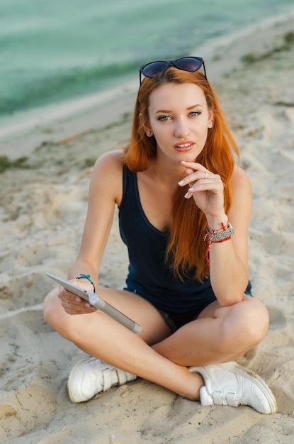 Mujer sexy pelirroja con tablet PC en una playa.