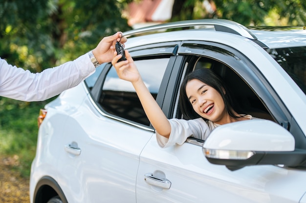 Una mujer se sienta en un automóvil y extiende su mano para recibir las llaves del automóvil.