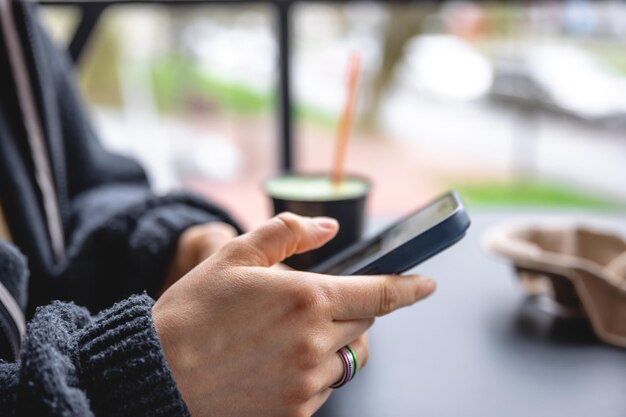 Una mujer se sienta en la terraza de un café y usa un teléfono inteligente cerrado