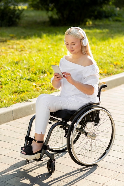 Mujer en silla de ruedas escuchando música al aire libre con smartphone
