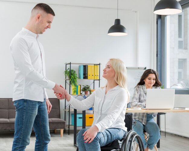 Mujer en silla de ruedas estrechándole la mano con un compañero de trabajo