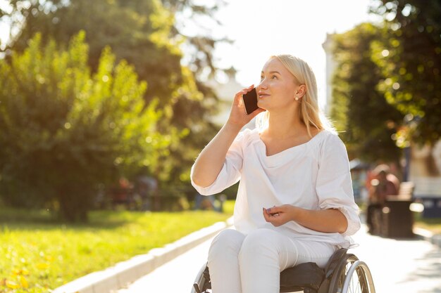 Mujer en silla de ruedas hablando por teléfono al aire libre