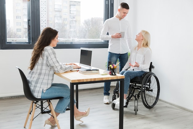 Foto gratuita mujer en silla de ruedas en la oficina con compañeros de trabajo