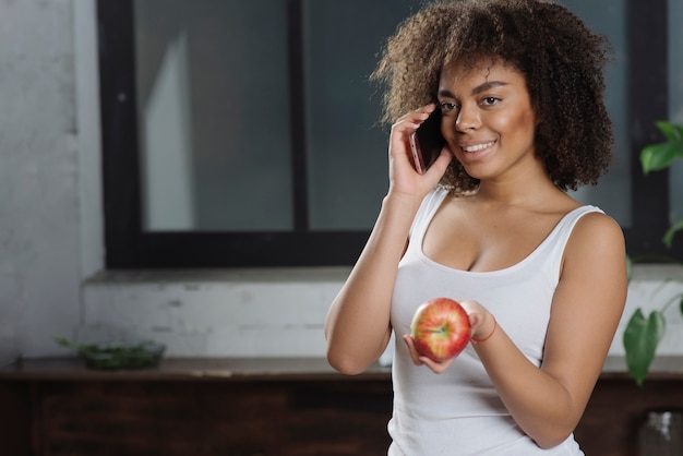 Foto gratuita mujer con smartphone y manzana en cocina