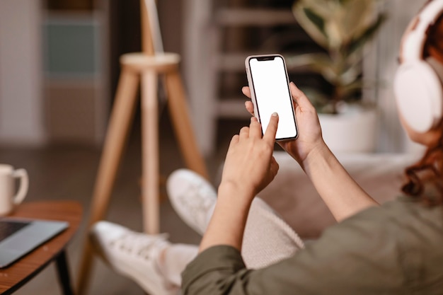 Mujer con smartphone moderno y auriculares en el sofá