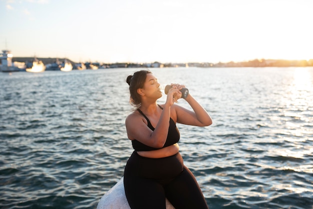 Mujer con sobrepeso que se hidrata con agua después de hacer ejercicio al aire libre