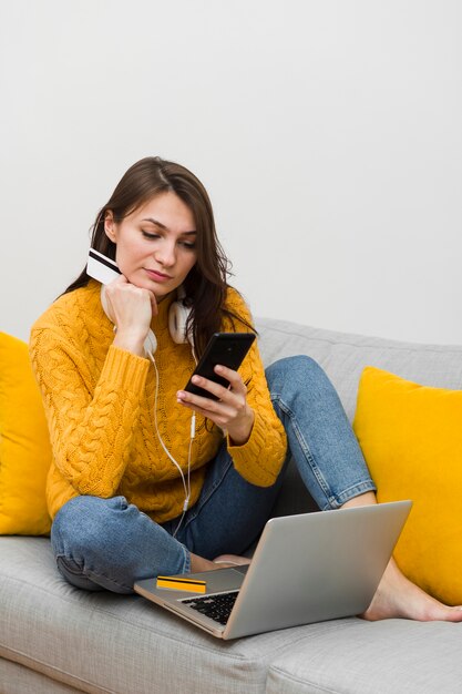 Mujer en el sofá mirando el teléfono inteligente y con tarjeta de crédito