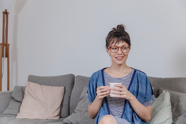 Foto gratuita mujer en sofá sujetando taza de café