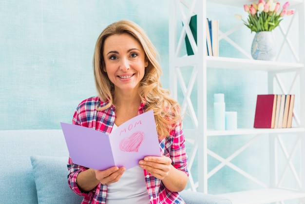 Mujer en sofá con tarjeta de felicitación con inscripción de mamá