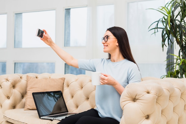 Mujer en sofá tomando selfie con café