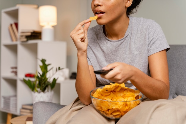 Mujer en el sofá viendo la televisión y comiendo patatas fritas