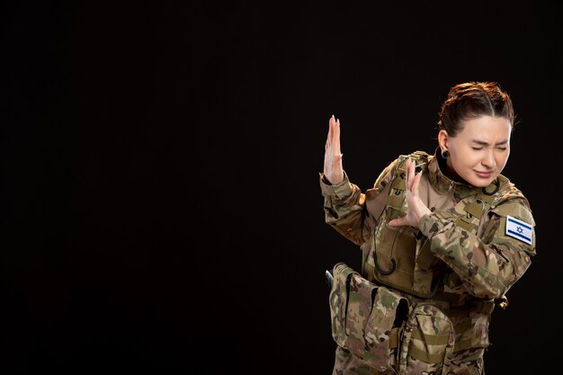 Mujer soldado en camuflaje en la pared negra