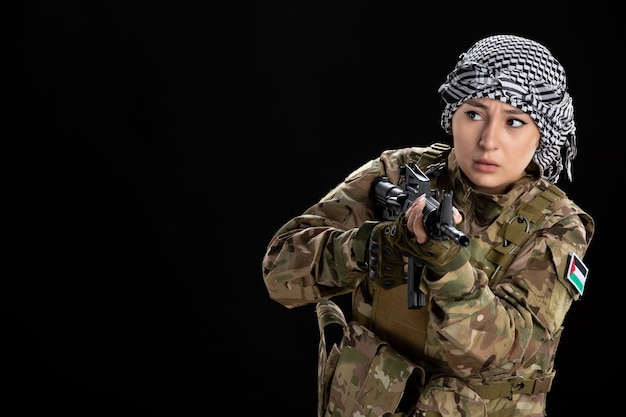 Foto gratuita mujer soldado en uniforme militar con el objetivo de ametralladora en la pared negra